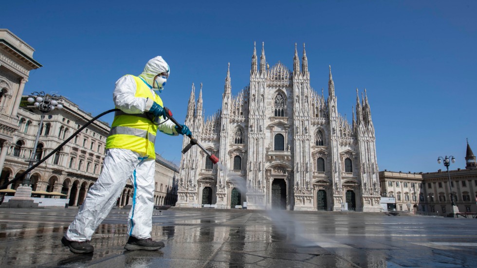En man sprejar desinfektionsmedel på ett ödsligt Piazza del Duomo i Milano.