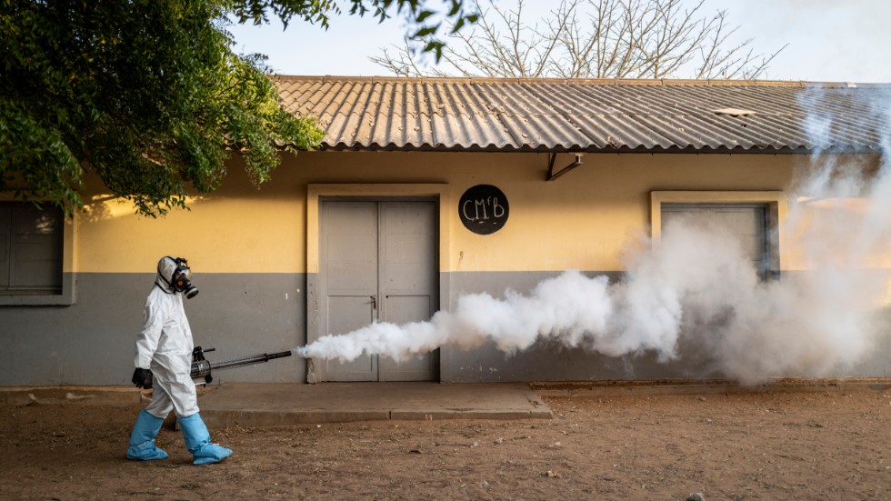 Byn Ngunta ligger både i Senegal och i Gambia. Båda länderna har drabbats av coronaviruset. På bilden ses en kommunanställd som sprutar desinfektionsmedel utanför en skola i Dakar i Senegal.