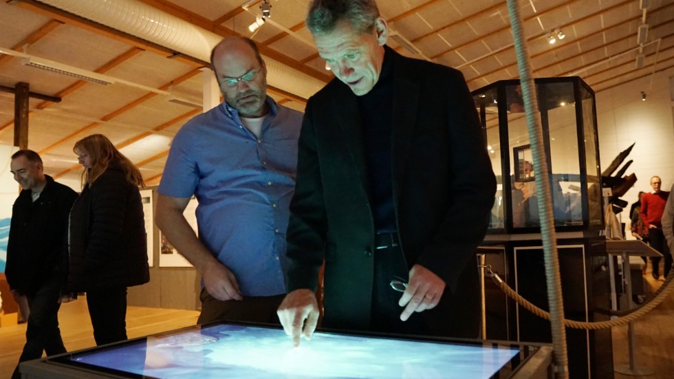 Ingemar Lundgren (t v) visar ett av visualiseringsborden för marinarkeologen Johan Rönnby. På skärmen syns en tredimensionell modell av vraket på havets botten.