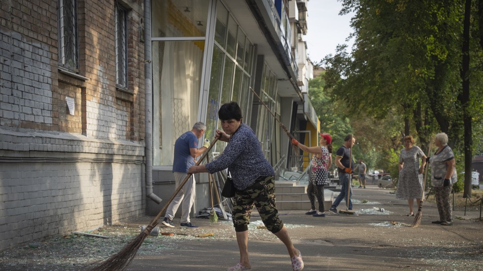 Invånare i Kiev städar upp krossat fönsterglas från gatan, efter att resterna av en rysk projektil slagit ned i området under natten till onsdag.