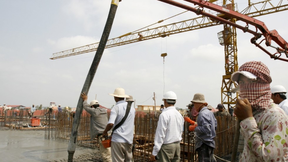 Byggnadsarbetare ser på medan cement fyller upp ett nytt lägenhetskomplex i Phnom Penh 2008. De senaste årtiondena har land- och huspriserna i huvudstaden skjutit i höjden.