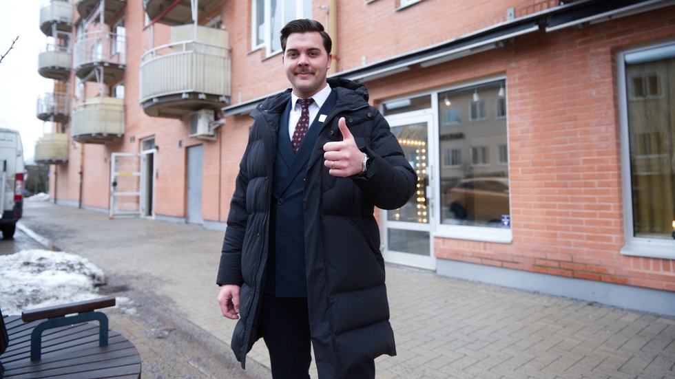 Mäklaren Kristian Horvath gör tummen upp för rekordförsäljningen av en bostadsrättslägenhet i Finspång. 
I bakgrunden syns fastigheten där lägenheten ligger. 