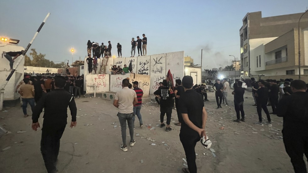 Demonstranter på en mur i närheten av Sveriges ambassad i Bagdad. I bakgrunden till höger syns rök stiga från ambassadkomplexet.