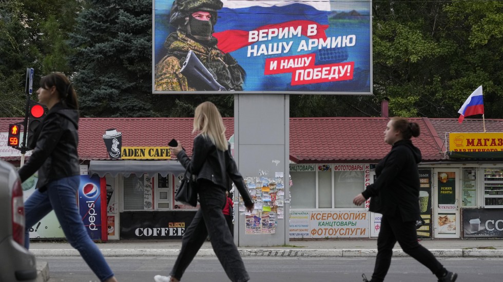 Luhanskbor promenerar förbi en anslagstavla med en bild på en rysk soldat och texten "Vi tror på vår armé och vår seger". Bild från 27 september.