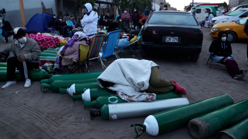 En man sover på tomma syrgasbehållare i väntan på att ett försäljningsställe i Villa El Salvador i Limas utkanter ska öppna. Bilden är från i torsdags.