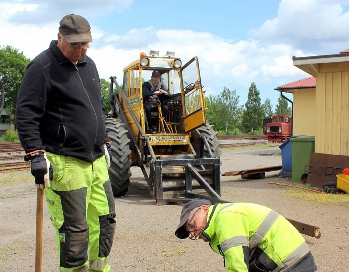 Göran Johansson står beredd med släggan medan Christer Jansson värmer järnet som ska böjas för att passa vid en järnvägsövergång. Oscar Nilsson väntar i lastmaskinen.