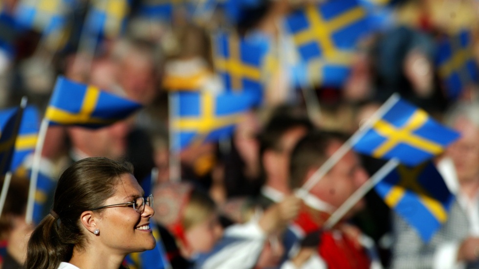 Bilden är tagen under ett av mellanåren. Svenska flaggans dag hade hunnit bli Sveriges nationaldag, men kronprinsessan har ännu ett leende på läpparna. Föga anar hon att riksdagen är på väg att avskaffa annandag pingst för att göra helgdag av 6 juni, på bekostnad av hela den svenska identiteten.