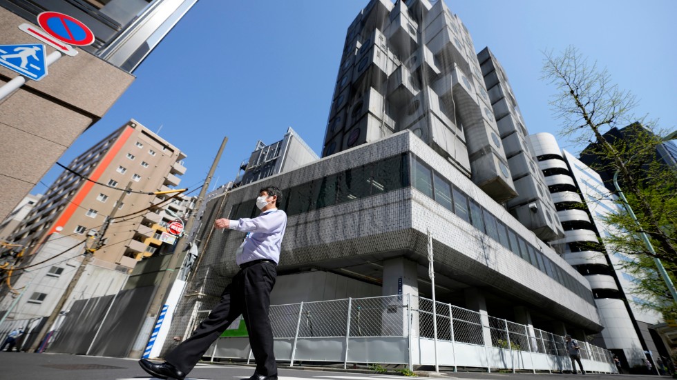 En man går förbi Nakagin-tornet i Tokyo, som nu försetts med nät och börjats monteras ner.