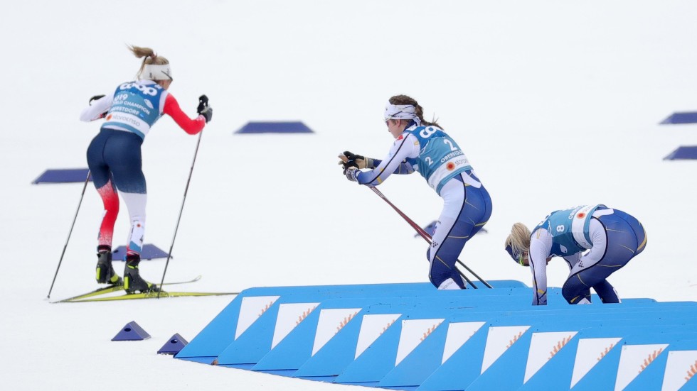 Sveriges Ebba Andersson, i mitten, strular med sina stavremmar under skidbytet i skiathlonloppet på VM i Oberstdorf. Vid bytet tappade Andersson dyrbara sekunder på Norges Therese Johaug, till vänster, som kunde dra ifrån och vinna guld. Arkivbild.