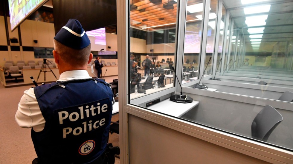 En polisman står invid de glasburar för anklagade i terrorrättegången i Bryssel. Glasburarna byts efter klagomål från försvaret ut och nu har rättegångsstarten försenats flera veckor. Arkivbild.