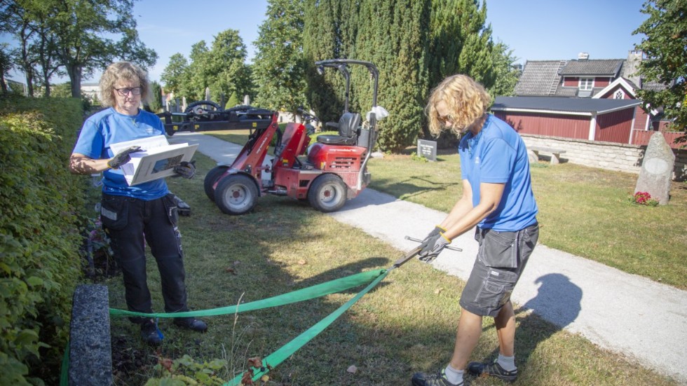 Kyrkogårdsarbetarna Ann Engström och Rosa Vatheuer kontrollerar gravstenarna. Här gör de dragtestet för att se om stenen står stadigt eller om den tippar. Bildäcket placerar de framför om det skulle vara så att stenen ramlar. 