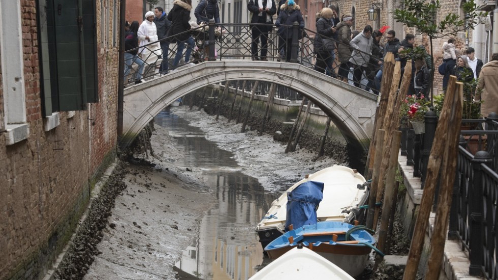 Turister på en av Venedigs många broar inspekterar de torra kanalerna den 21 februari.