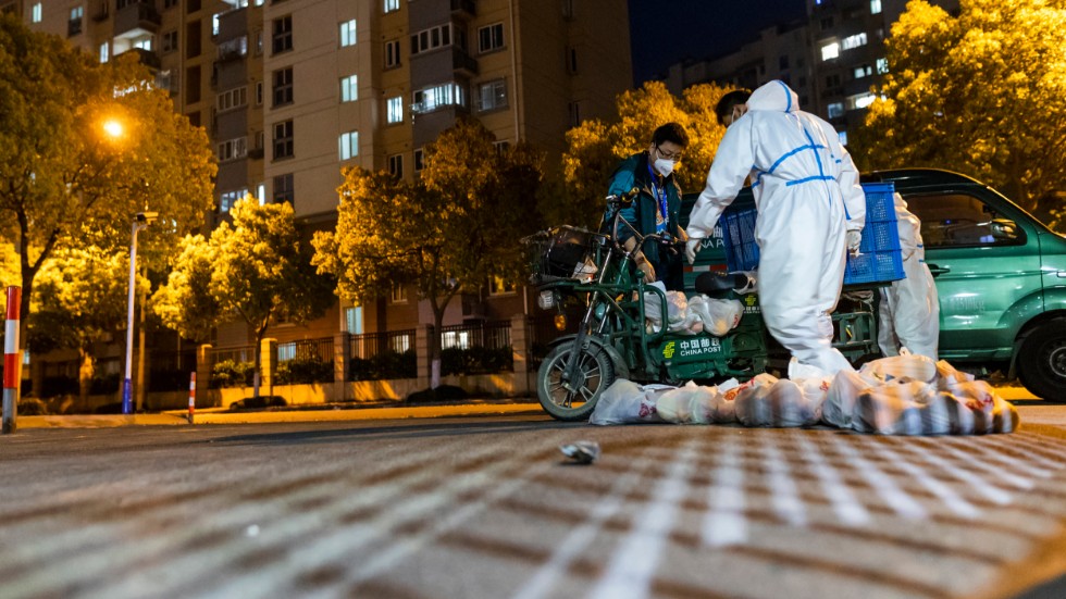 Personer i skyddskläder tar emot mat som levererats till ett bostadsområde i Shanghai. Arkivbild.